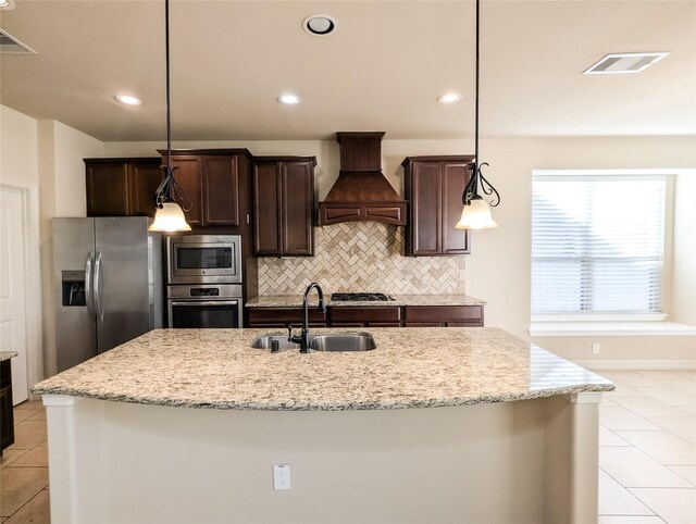 kitchen with appliances with stainless steel finishes, sink, custom exhaust hood, and a center island with sink