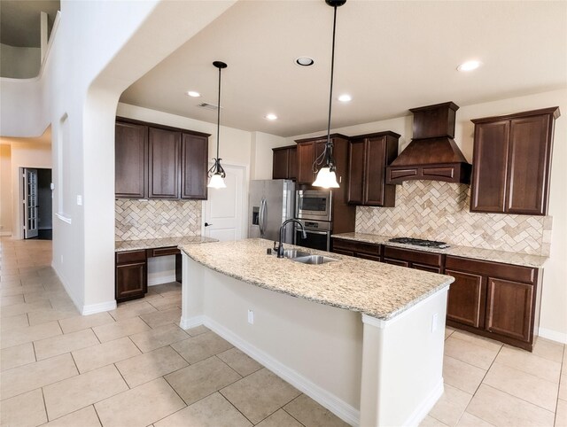 kitchen with sink, appliances with stainless steel finishes, a kitchen island with sink, hanging light fixtures, and custom range hood