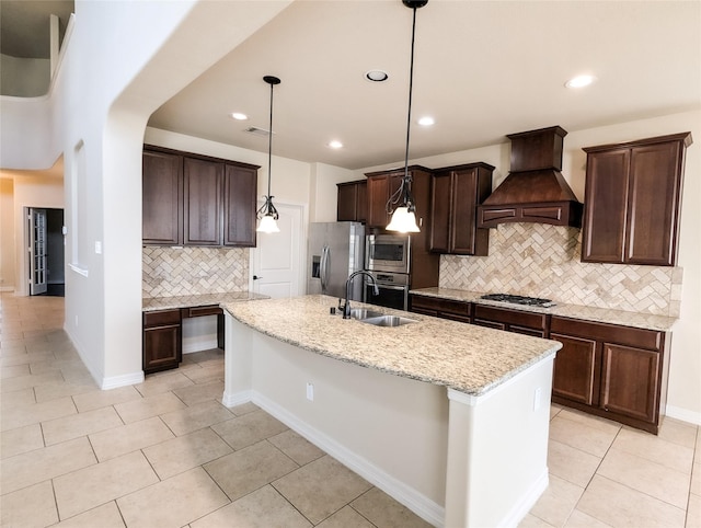 kitchen featuring a kitchen island with sink, stainless steel appliances, a sink, custom exhaust hood, and decorative light fixtures