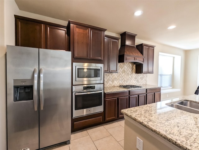 kitchen with sink, decorative backsplash, custom exhaust hood, light stone counters, and stainless steel appliances