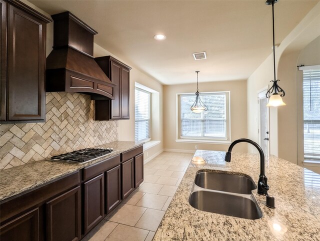 kitchen featuring stainless steel gas cooktop, sink, light stone counters, custom range hood, and pendant lighting