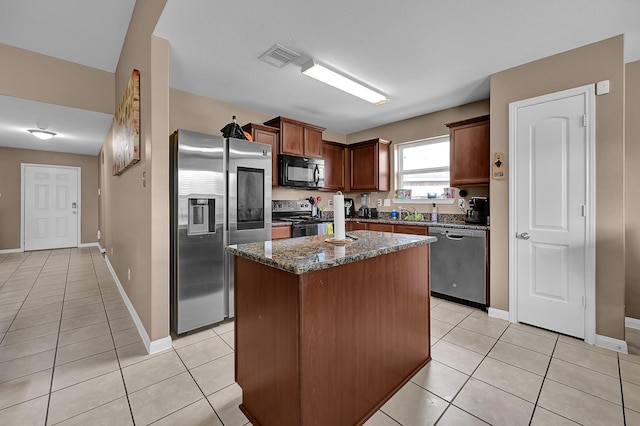 kitchen featuring appliances with stainless steel finishes, light tile patterned floors, a kitchen island, and dark stone counters