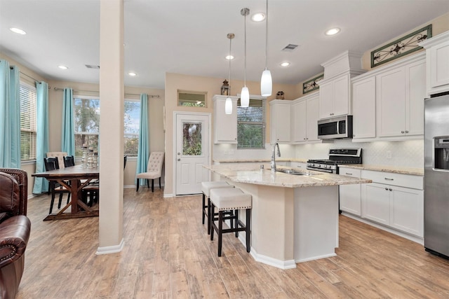 kitchen with pendant lighting, white cabinets, stainless steel appliances, light stone countertops, and a center island with sink