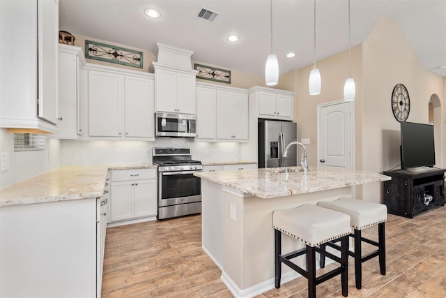 kitchen with white cabinetry, light hardwood / wood-style flooring, an island with sink, pendant lighting, and stainless steel appliances