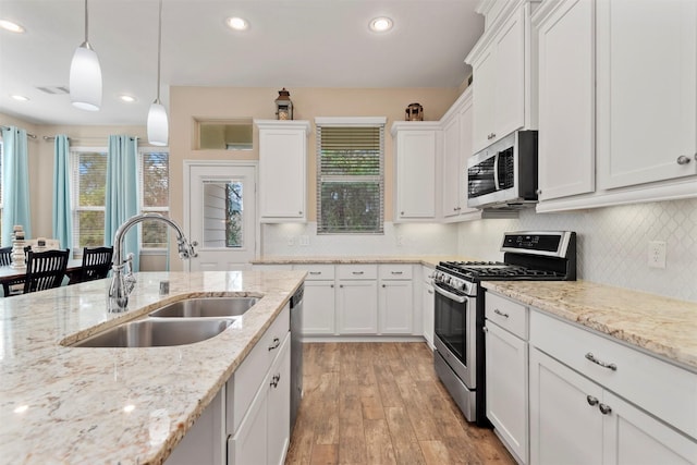 kitchen featuring sink, light hardwood / wood-style flooring, appliances with stainless steel finishes, white cabinets, and decorative light fixtures