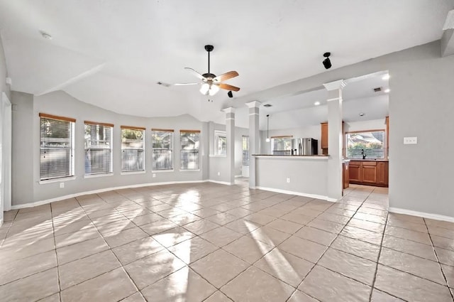 unfurnished living room featuring ornate columns, vaulted ceiling, a wealth of natural light, and ceiling fan