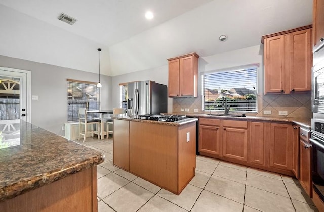 kitchen with lofted ceiling, sink, dark stone countertops, appliances with stainless steel finishes, and a kitchen island