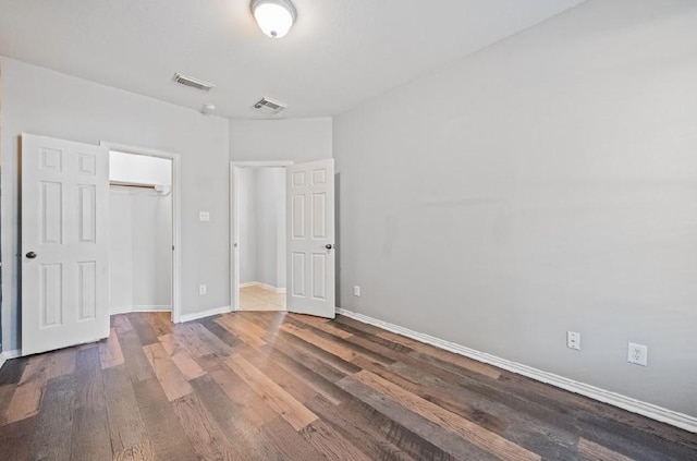 unfurnished bedroom with a walk in closet, dark wood-type flooring, and a closet