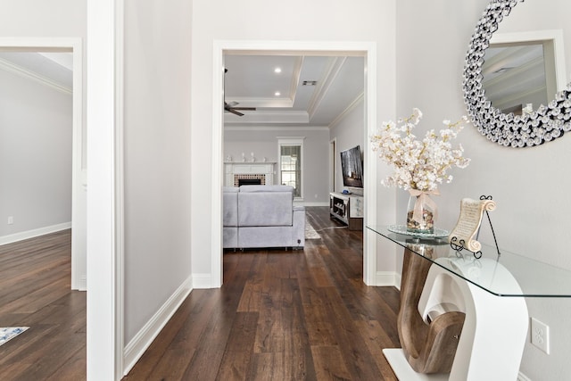 corridor featuring dark wood-type flooring, ornamental molding, and a raised ceiling