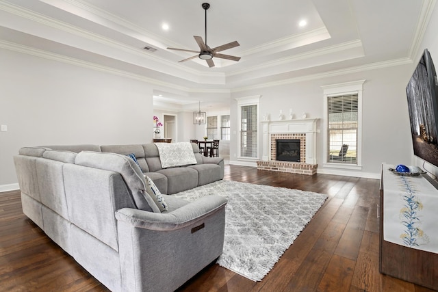 living room with ceiling fan, a brick fireplace, dark hardwood / wood-style flooring, and a tray ceiling