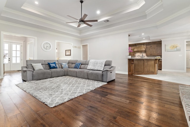 living room with dark wood-type flooring, ceiling fan, a tray ceiling, and crown molding