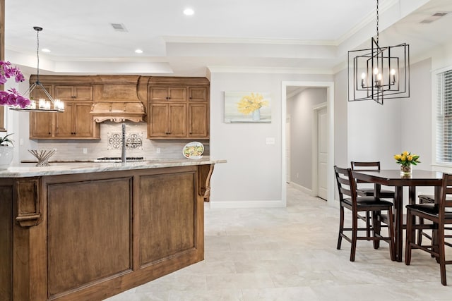 kitchen featuring hanging light fixtures, crown molding, light stone counters, and decorative backsplash