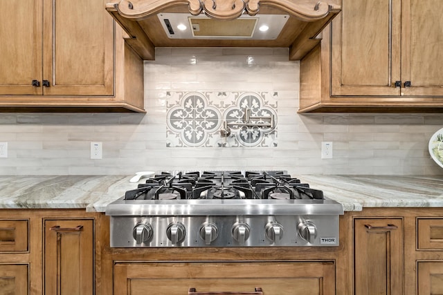 kitchen featuring stainless steel gas stovetop, exhaust hood, light stone counters, and decorative backsplash