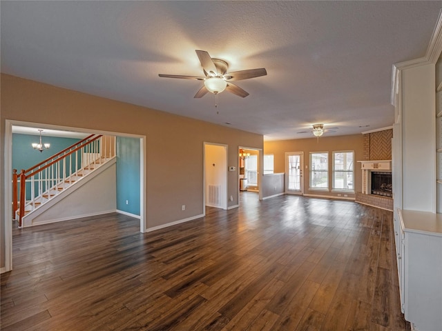 unfurnished living room featuring a brick fireplace, ceiling fan with notable chandelier, dark hardwood / wood-style floors, and a textured ceiling