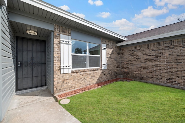 entrance to property featuring brick siding and a lawn