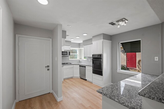 kitchen with white cabinetry, appliances with stainless steel finishes, light wood-type flooring, and dark stone countertops