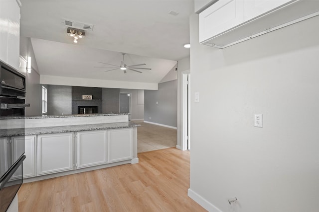 kitchen with light stone counters, a fireplace, a ceiling fan, visible vents, and white cabinets