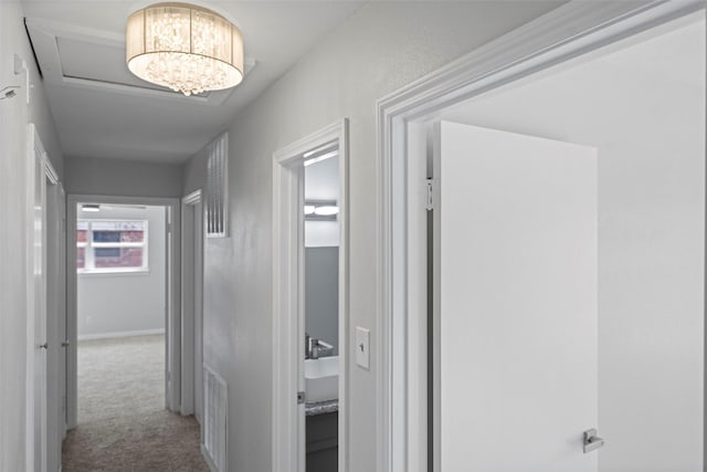 corridor featuring light colored carpet, visible vents, and an inviting chandelier