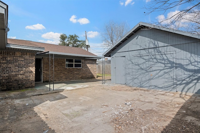 exterior space with a shingled roof, an outbuilding, and brick siding