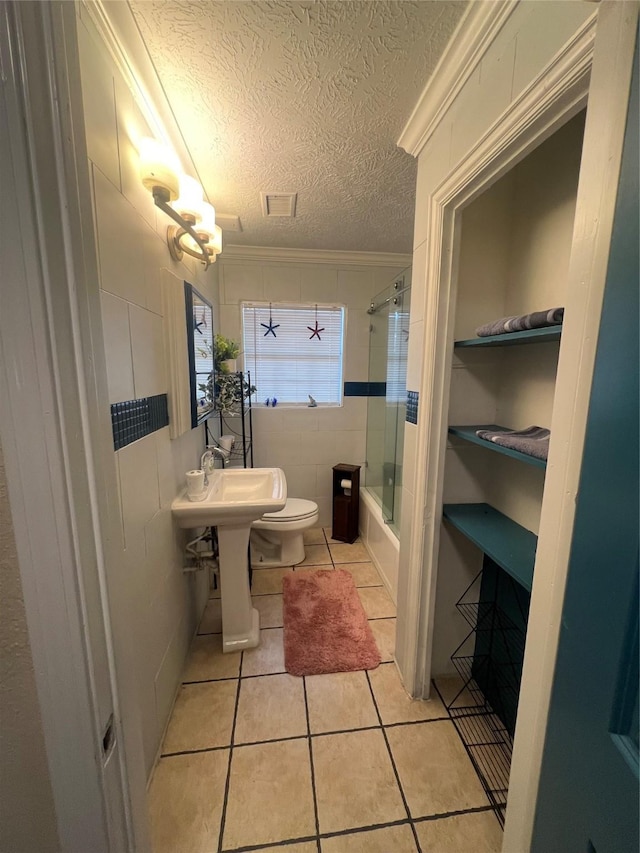 bathroom featuring crown molding, combined bath / shower with glass door, a textured ceiling, tile patterned floors, and toilet