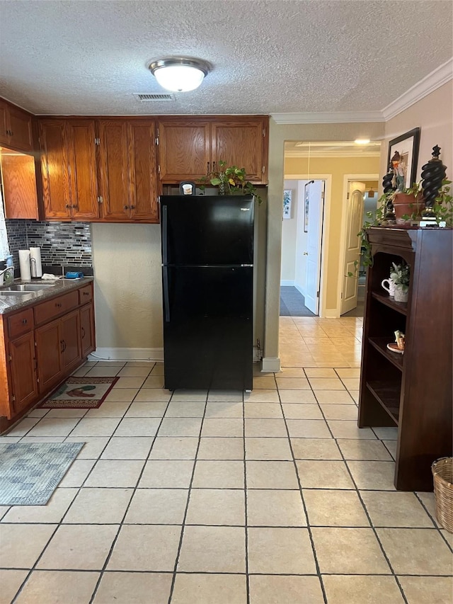 kitchen with black fridge, tasteful backsplash, a textured ceiling, light tile patterned floors, and ornamental molding