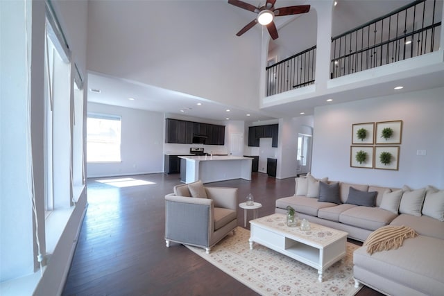 living area with recessed lighting, a high ceiling, ceiling fan, wood finished floors, and baseboards