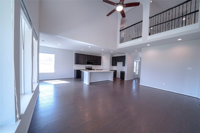 unfurnished living room with dark wood-style flooring, a high ceiling, ceiling fan, and baseboards