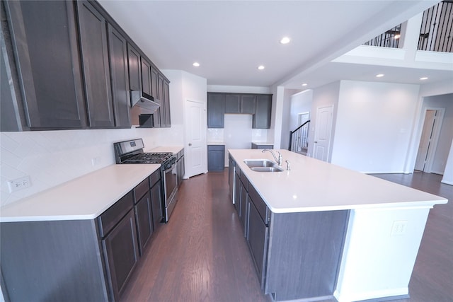 kitchen with under cabinet range hood, a sink, decorative backsplash, dark wood-style floors, and gas range