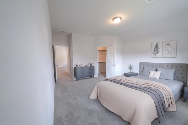 bedroom featuring a walk in closet, a closet, visible vents, and light carpet