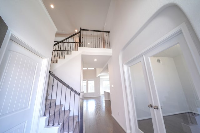 stairs with recessed lighting, wood finished floors, visible vents, a towering ceiling, and baseboards