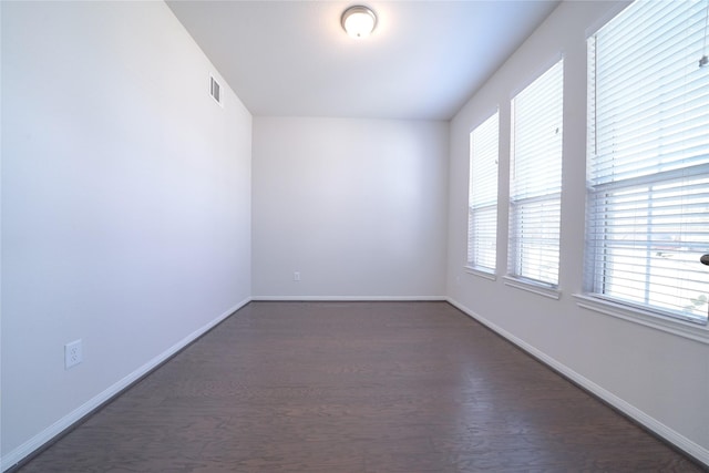 unfurnished room featuring dark wood-style floors, visible vents, and baseboards