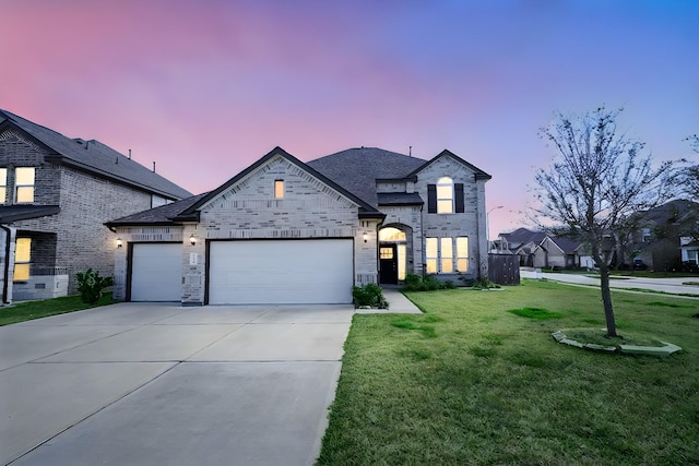 french country inspired facade featuring a garage, driveway, a lawn, and brick siding