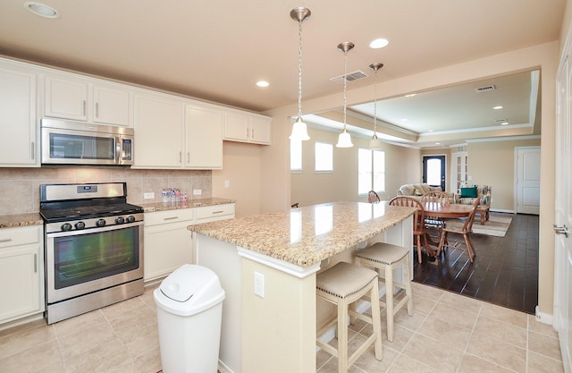 kitchen with a center island, appliances with stainless steel finishes, a raised ceiling, and white cabinets