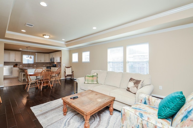 living room with crown molding, dark wood-type flooring, sink, and a tray ceiling