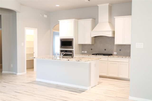 kitchen with white cabinetry, premium range hood, a kitchen island with sink, and stainless steel appliances