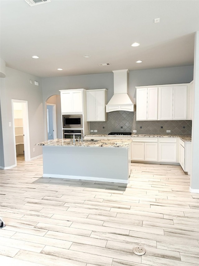 kitchen featuring white cabinetry, premium range hood, appliances with stainless steel finishes, and a kitchen island with sink