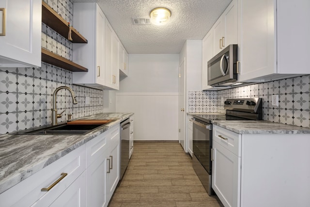 kitchen with a sink, visible vents, white cabinets, appliances with stainless steel finishes, and open shelves