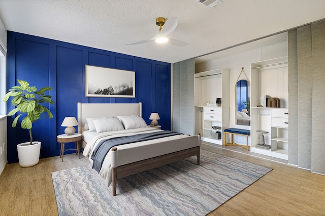 bedroom featuring visible vents, a decorative wall, light wood-style flooring, and ceiling fan