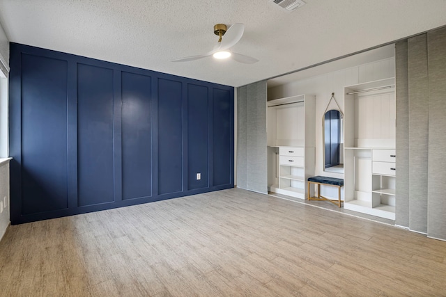 unfurnished bedroom featuring a textured ceiling, visible vents, light wood-style flooring, and a decorative wall