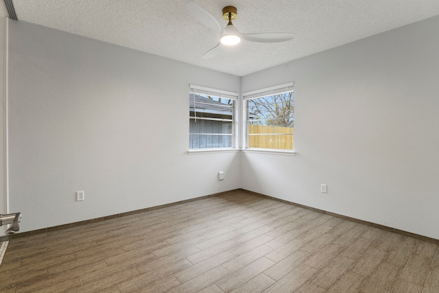 empty room featuring ceiling fan, a textured ceiling, baseboards, and wood finished floors