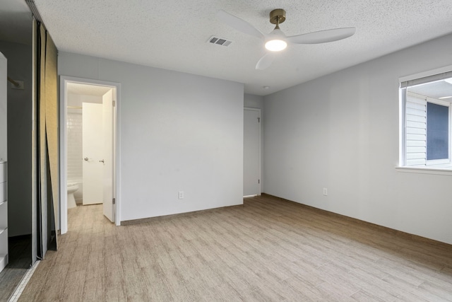 unfurnished bedroom featuring a textured ceiling, ensuite bathroom, a ceiling fan, visible vents, and light wood-type flooring