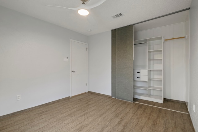 unfurnished bedroom with ceiling fan, a closet, wood finished floors, and visible vents