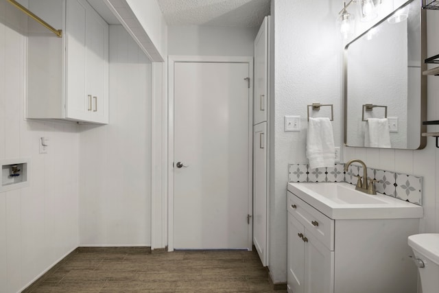 bathroom featuring a textured ceiling, toilet, wood finished floors, vanity, and tasteful backsplash