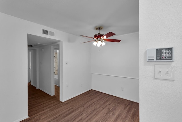 empty room with a ceiling fan, wood finished floors, visible vents, and baseboards