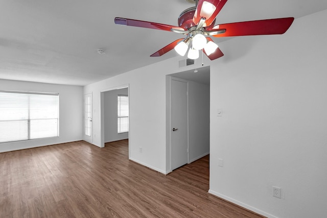 empty room featuring a wealth of natural light, visible vents, baseboards, and wood finished floors