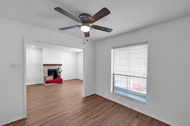 empty room with ceiling fan, a fireplace, baseboards, and wood finished floors