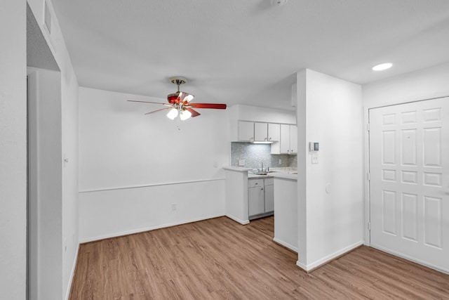 kitchen featuring baseboards, a ceiling fan, light wood-style flooring, light countertops, and backsplash