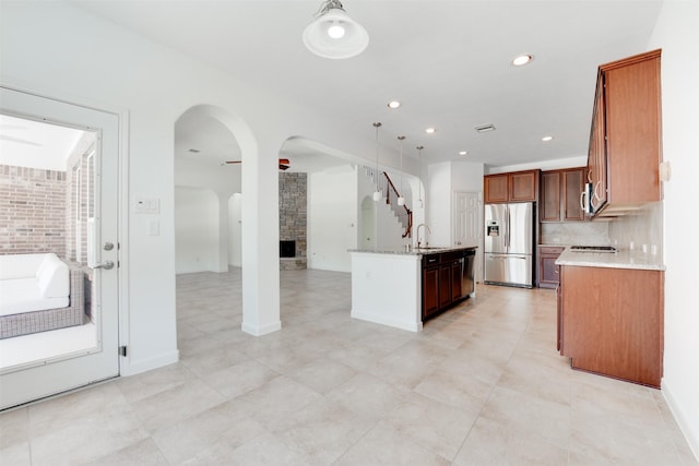 kitchen featuring sink, tasteful backsplash, a center island with sink, stainless steel fridge, and light stone countertops