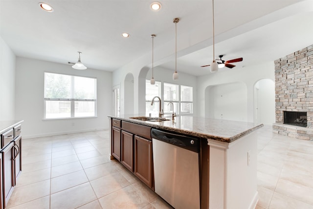 kitchen featuring an island with sink, sink, hanging light fixtures, stainless steel dishwasher, and light stone counters