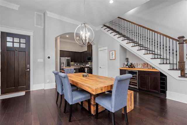 dining space with dark hardwood / wood-style floors, beverage cooler, a chandelier, ornamental molding, and bar